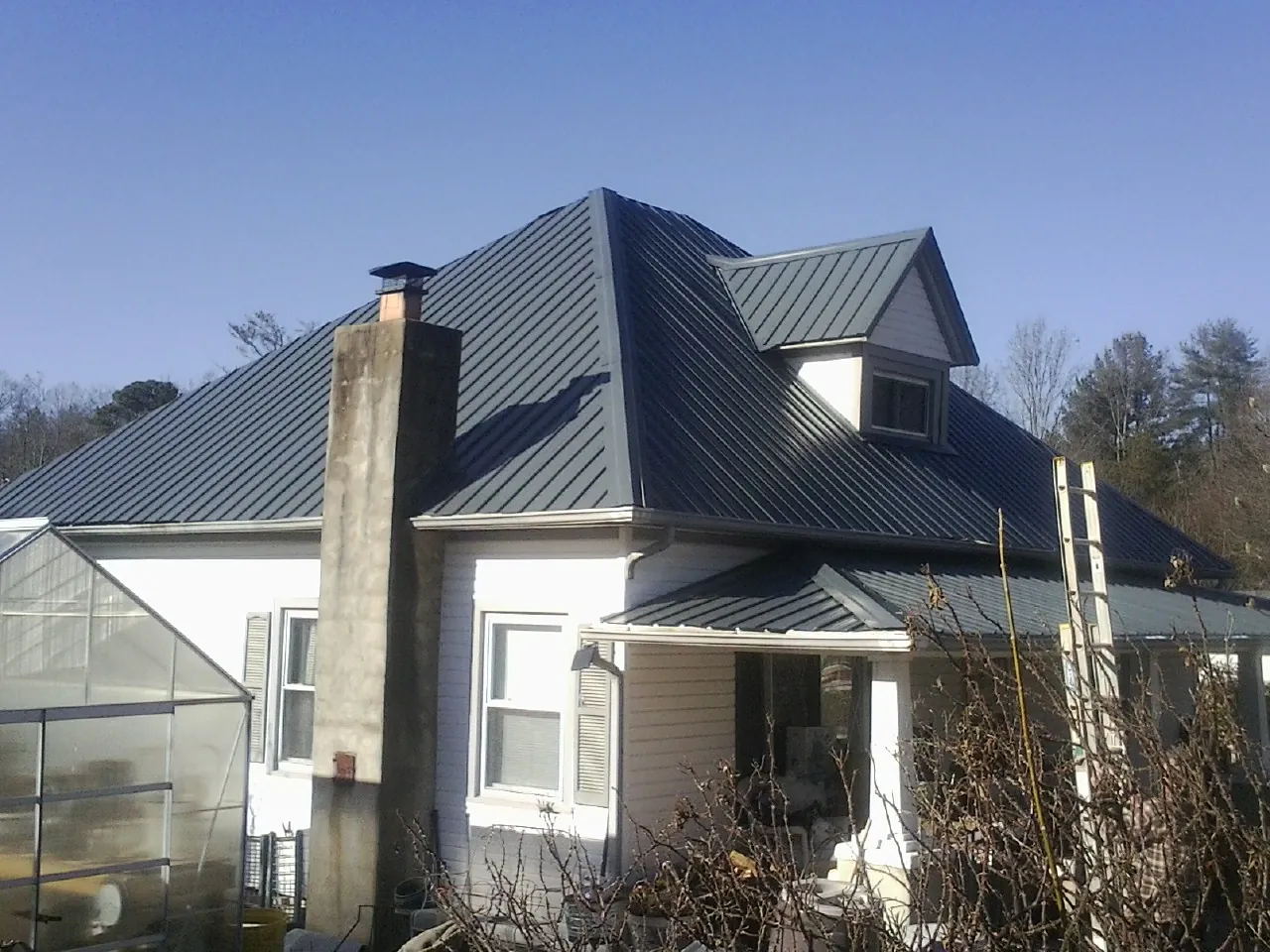 Dark blue standing seam metal roof on a white farmhouse with dormer — Slate & Tile Roof Repair by Roofing Brothers in Sproul