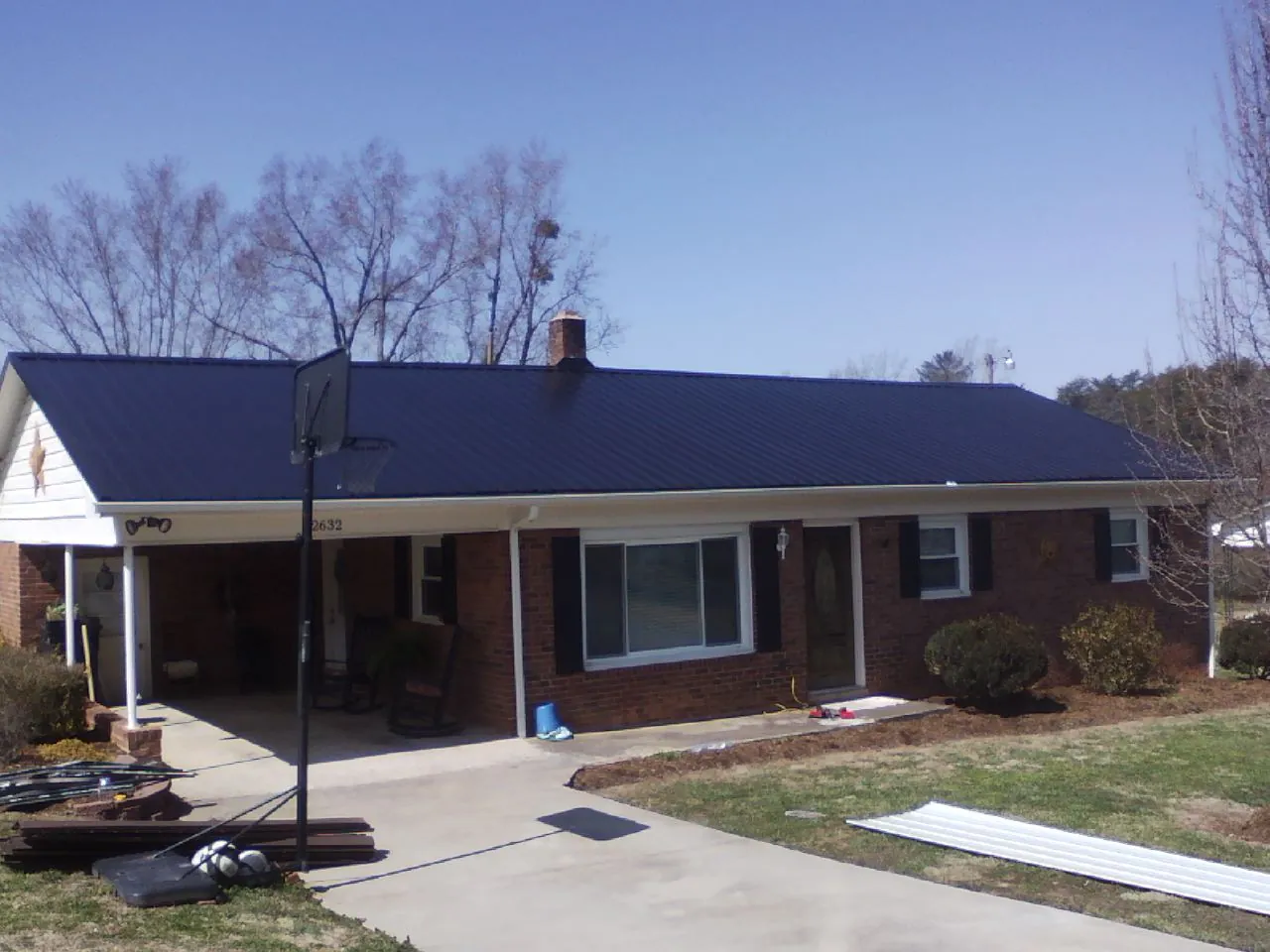 Finished dark blue metal roof on a brick ranch with a carport in Sproul