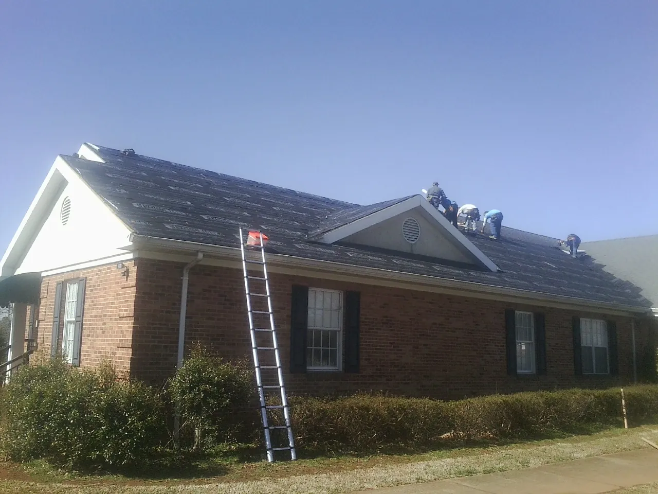 Crew tearing shingles off a brick ranch roof with a ladder set — Emergency Roof Repair work by our crew in Sproul