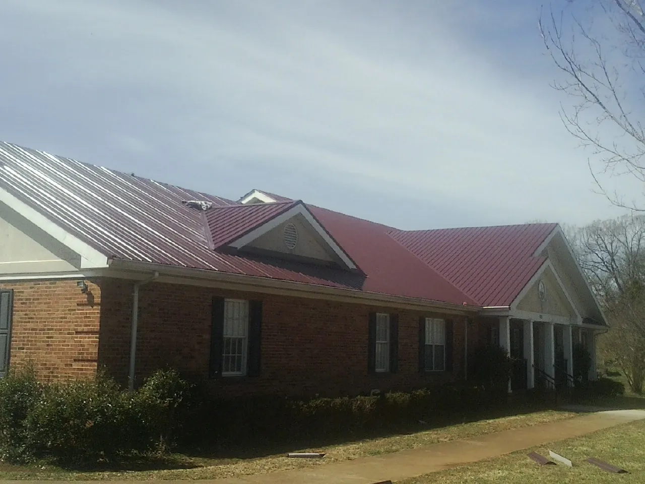 Red metal roof with gabled entries on a long brick building, from a Hail Damage Roof Repair job in Sproul