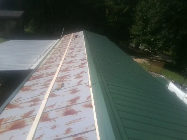 Old rusted panels beside newly installed green metal roofing — Wind Damage Roof Repair by Roofing Brothers in Sproul