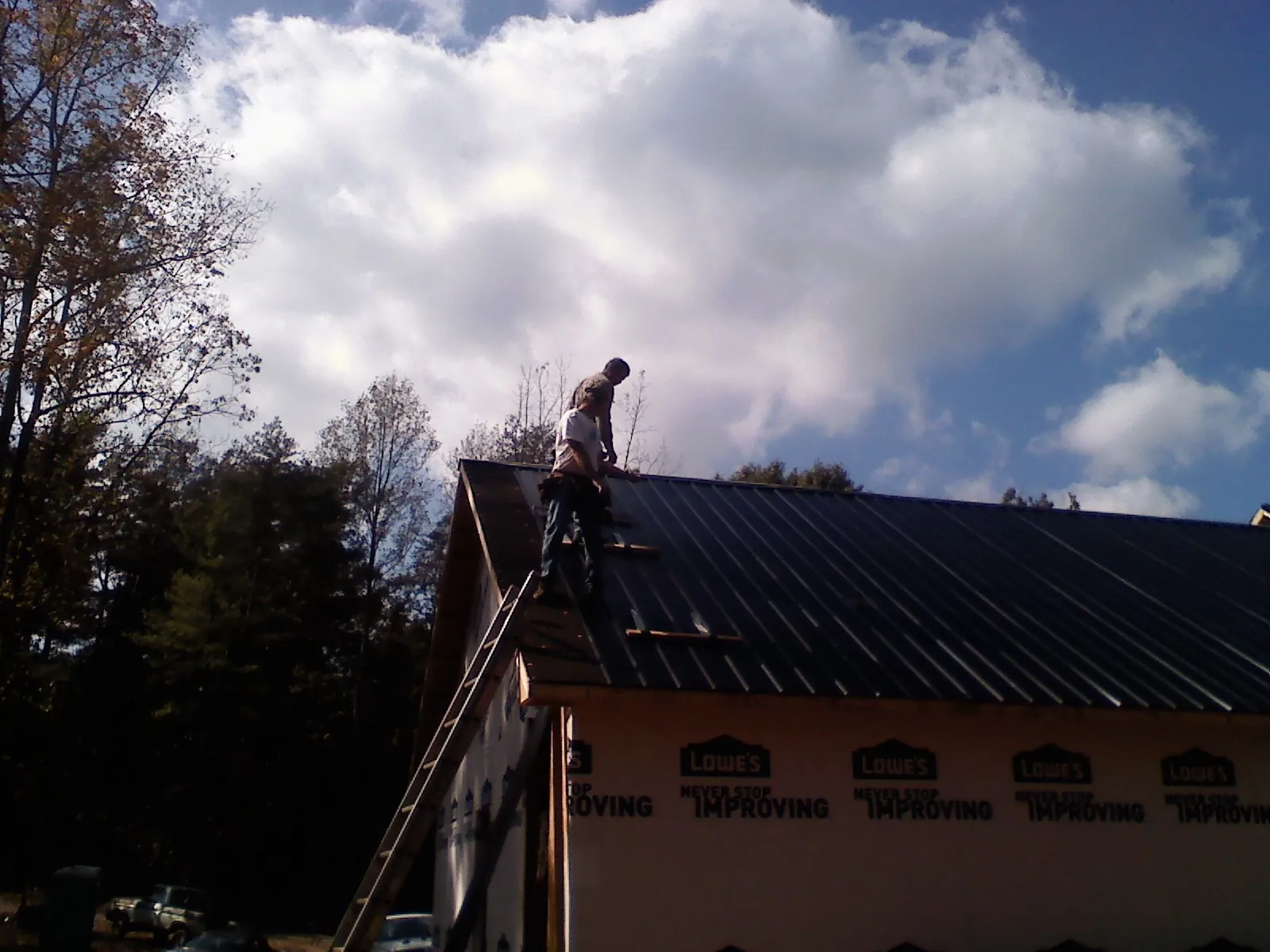 Roofer fastening dark metal panels high against a cloudy sky, from a Roof Inspection job in Sproul