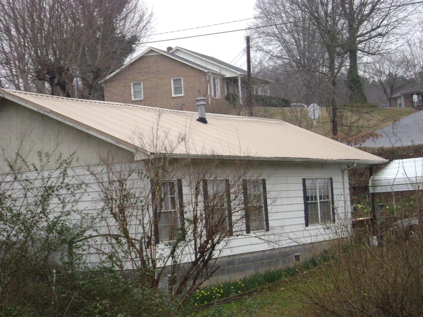 Tan metal roof on a white sided house set into a hillside — Commercial Roofing by Roofing Brothers in Sproul