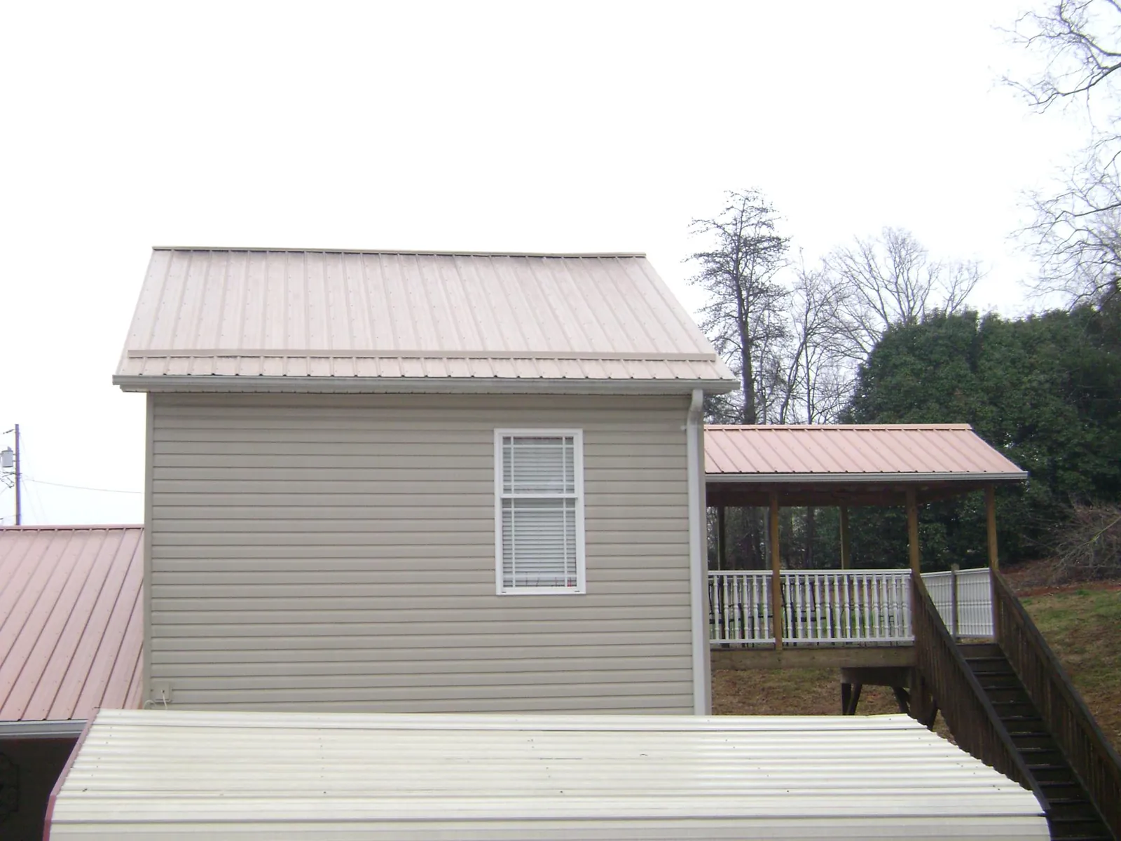 Tan metal roofs on a two story addition and attached porch, from a Roof Replacement job in Sproul